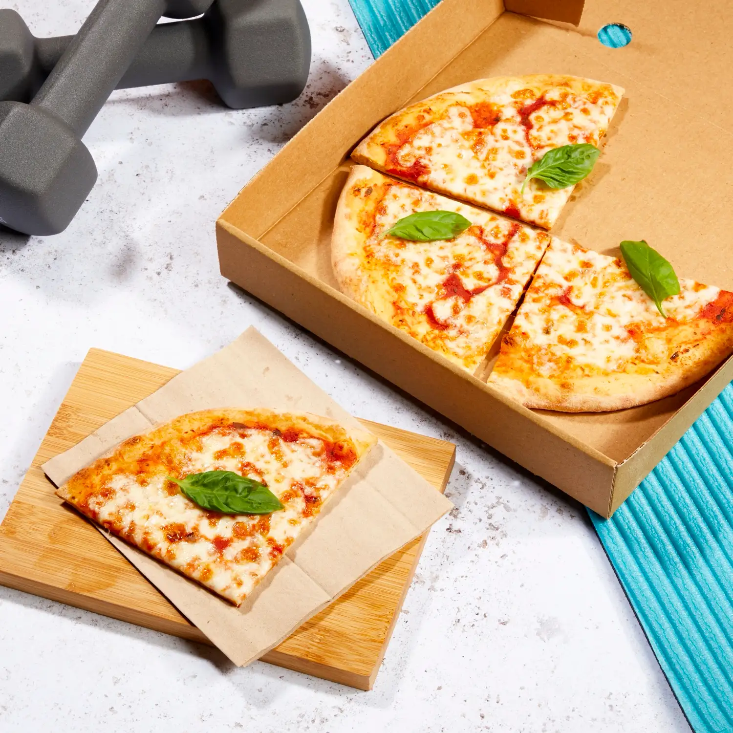 An open Protein Pizza Co. box beside dumbbells and a gym towel