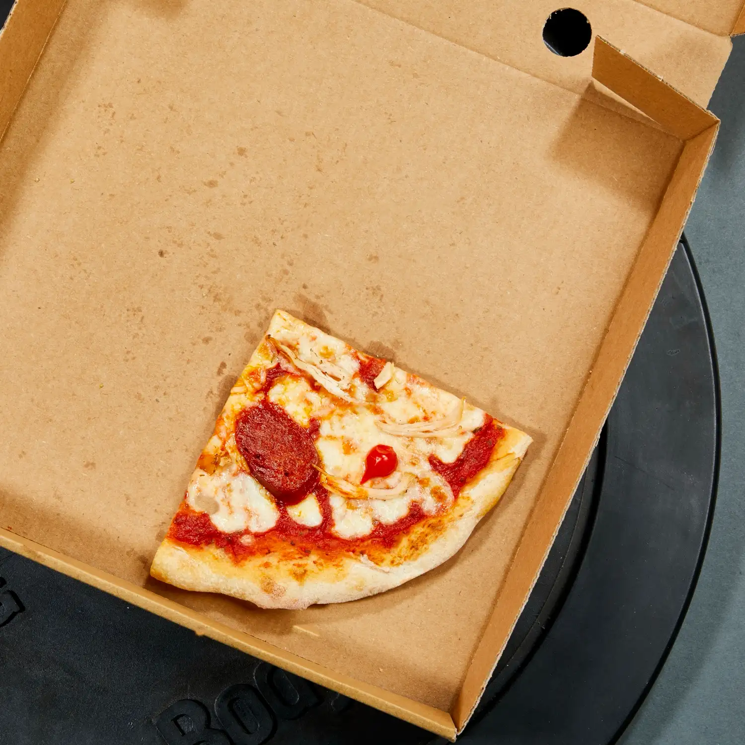 The last slice in a Protein Pizza Co. box, resting on a weight plate